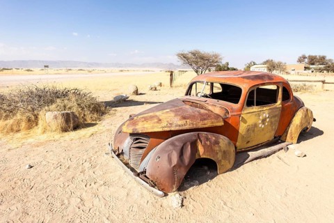 Solitaire's car graveyard in Namibia features rusted vintage cars near small desert buildings, set