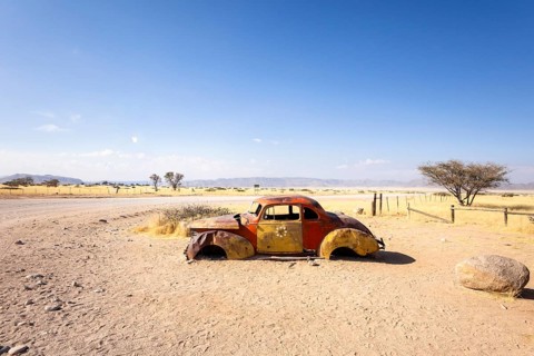 Solitaire's car graveyard in Namibia features rusted vintage cars near small desert buildings, set