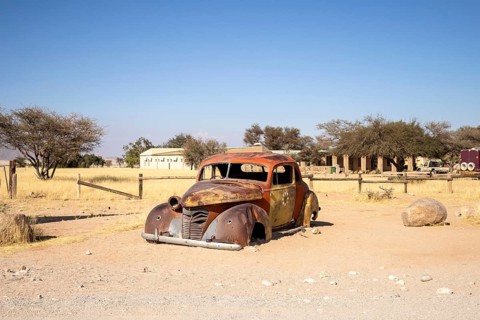 Solitaire's car graveyard in Namibia features rusted vintage cars near small desert buildings, set
