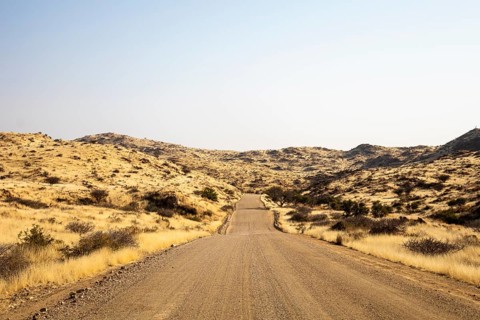 A road Spreetshoogte Pass in Namibia, with a gravel road winding through golden grassland and rocky
