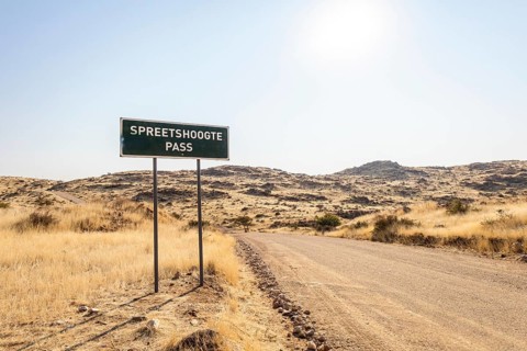 A road sign marks Spreetshoogte Pass in Namibia, with a gravel road winding through golden
