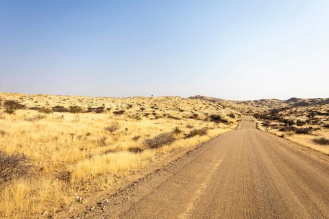A road Spreetshoogte Pass in Namibia, with a gravel road winding through golden grassland and rocky