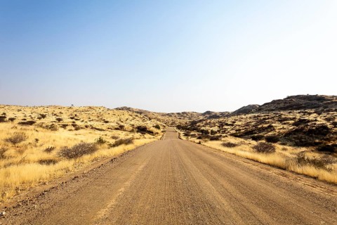 A road Spreetshoogte Pass in Namibia, with a gravel road winding through golden grassland and rocky