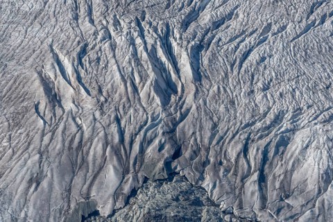 Crevasses and streaks mark the surface of the glacier. The sunlight highlights these unique