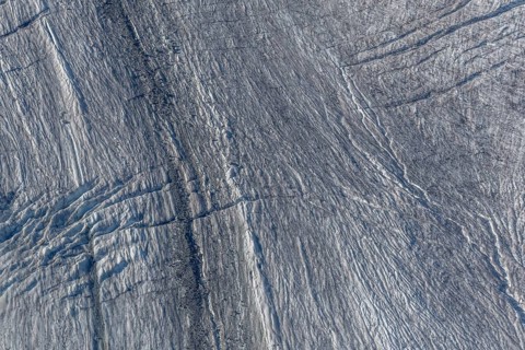 Crevasses and streaks mark the surface of the glacier. The sunlight highlights these unique
