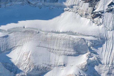 A large blanket of snow covers the rocks in the mountains. The sky is clear and reflects the serene