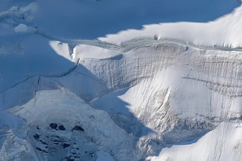A large blanket of snow covers the rocks in the mountains. The sky is clear and reflects the serene