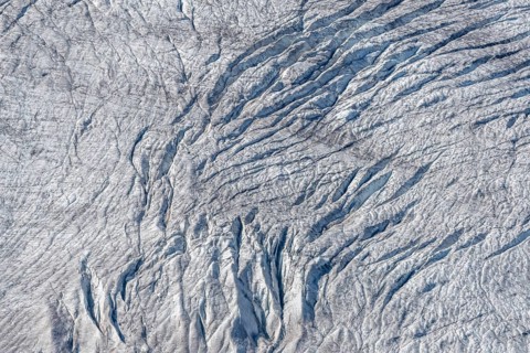 Crevices mark the surface of the glacier. The landscape is illuminated by daylight, highlighting