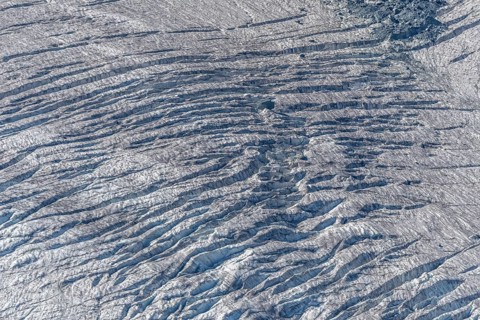 Crevices mark the surface of the glacier. The landscape is illuminated by daylight, highlighting