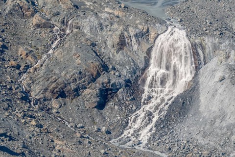 Waterfalls flow over a glacier surrounded by rocks and debris. This natural phenomenon is caused by