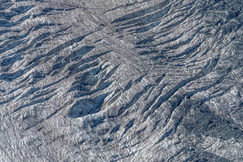 Crevices mark the surface of the glacier. The landscape is illuminated by daylight, highlighting