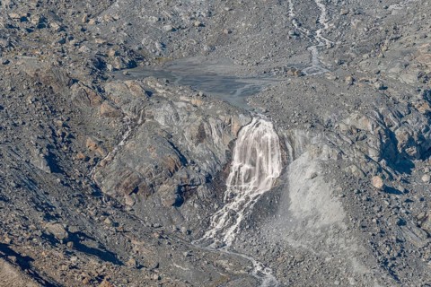 Waterfalls flow over a glacier surrounded by rocks and debris. This natural phenomenon is caused by