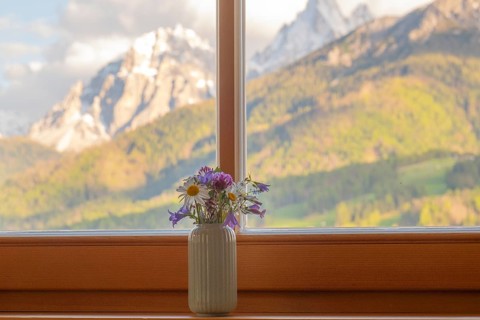 A vase with meadow flowers stands on the windowsill in the background the mountains of the