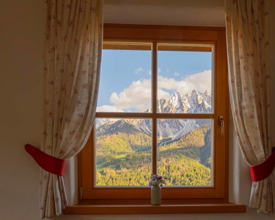 View through a window to the Dolomites in the foreground a small vase with meadow flowers on the