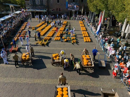 A large traditional Dutch cheese market with arrangement of cheese and people standing around,