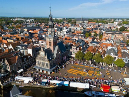 Historic city view with a tower and a busy cheese market in the old town centre, aerial view,