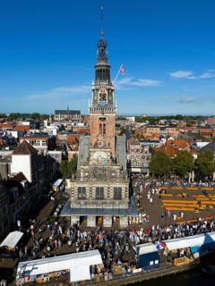 Imposing clock tower with lively market activity and market stalls in the foreground, under blue