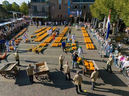Traditional market with cheese wagon and participants, crowds and historic building in the