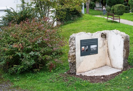 Memorial plaque with photos of a former concentration camp inmate, remains of the walls of a