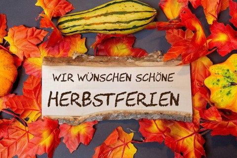 (photomontage) : Wooden sign with the inscription WIR WÜSCHEN SCHÖNE HERBSTFERIEN and autumnal