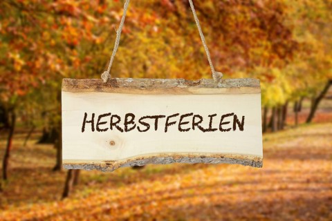 (photomontage) : Wooden sign with the inscription HERBSTFERIEN in front of an autumn-coloured