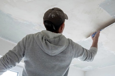 Plasterer levelling and smoothing the ceiling in the interior