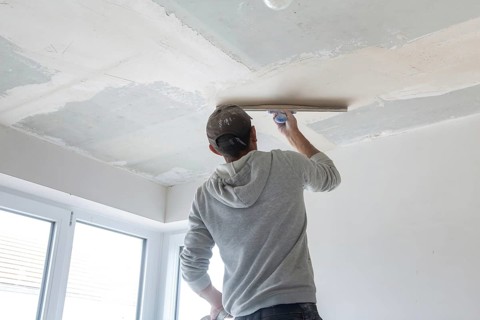 Plasterer levelling and smoothing the ceiling in the interior