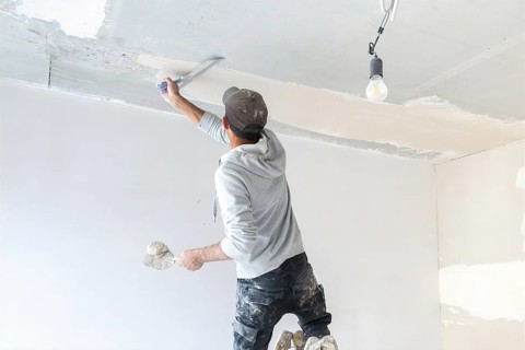 Plasterer levelling and smoothing the ceiling in the interior