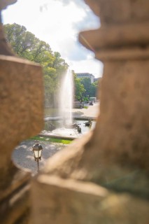 A fountain spouts water through an opening in a wall in a sunny park, Munich, Germany