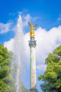 Golden statue on column with fountain and trees in front of blue sky, Munich, Germany