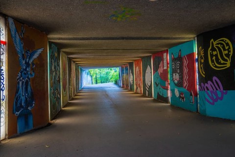A graffiti-covered tunnel leads to a green open-air area, Munich, Germany