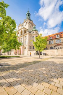 Mesmerising building surrounded by spring trees under a blue sky and paved area, Munich, Germany