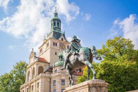 Equestrian statue in front of a magnificent historical building, surrounded by trees and blue sky,
