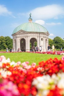 Flowery pavilion with green dome in front of a colourful flower bed and under a blue sky, Munich,