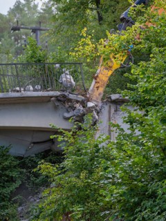 An excavator working on the end of a bridge, surrounded by dense greenery, bridge demolition, Calw,