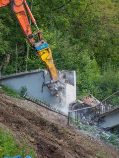 An excavator smashes concrete, dust rises, railings come loose, bridge demolition, Calw, Germany