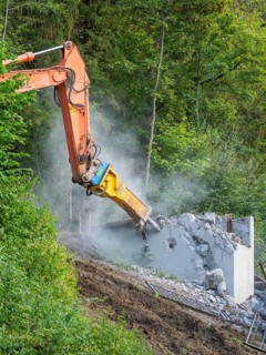 An excavator breaks a concrete wall in a green environment, dust rises, bridge demolition, Calw,