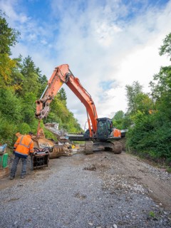 A worker and an excavator carry out work on a road covered with gravel, bridge demolition, Calw,