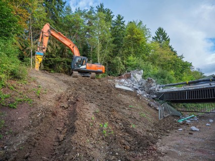 An excavator works on a demolished bridge in a wooded area, bridge demolition, Calw, Germany