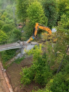 An excavator works on the demolition of a bridge from above in a forest area, bridge demolition,