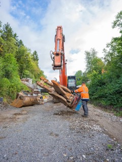 A worker uses an excavator to carry out work on tree trunks on ballast, bridge demolition, Calw,