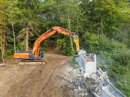 An excavator demolishes a wooden bridge in a wooded area, bridge demolition, Calw, Germany
