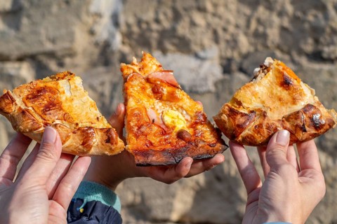 Three slices of maltese pizza hold in the hands of mother and son with stone background, Gozo,