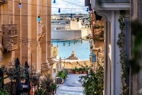 Charming downhill street illuminated with colorful bulbs in Valletta, Malta. St Angelo Fortress in