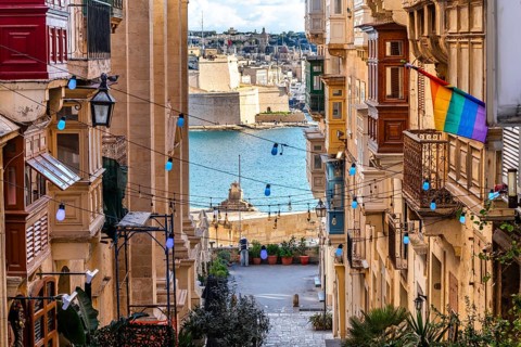 Charming downhill street illuminated with colorful bulbs in Valletta, Malta. St Angelo Fortress in