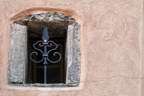Small window with grille in an old building with pink-coloured plaster, Alsace, France