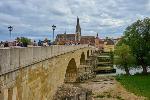 People walking across a historic bridge with a view of the cathedral and trees, Stone Bridge,