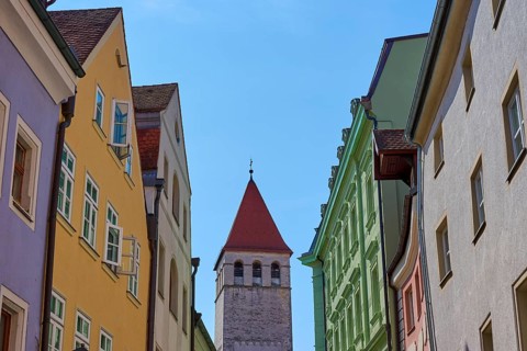 Colourful buildings and church tower along a busy street under a clear sky, Regensburg, Bavaria,