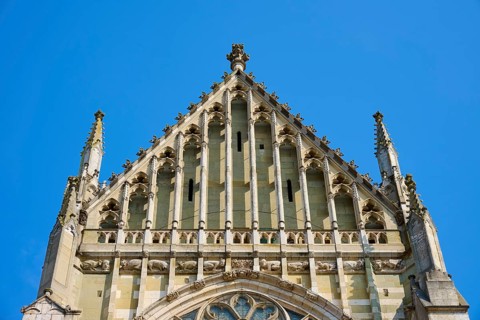 Decorated Gothic façade with window and roof spire under a clear sky, St Peter's Cathedral,
