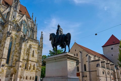 Equestrian statue in front of a historic church under a blue sky, St Peter's Cathedral, Regensburg,
